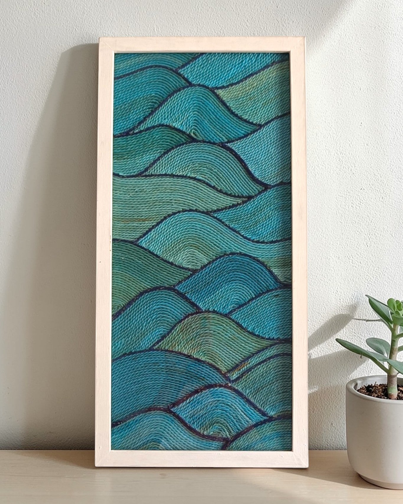 Framed artwork with wavy blue pattern made from fishing net on a white wall